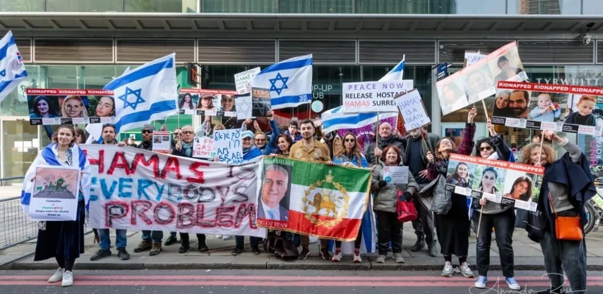A line of people stretches across a pavement behind a hand painted banner reading Hamas Everybody’s Problem, Israeli and Iranian flags at either end.