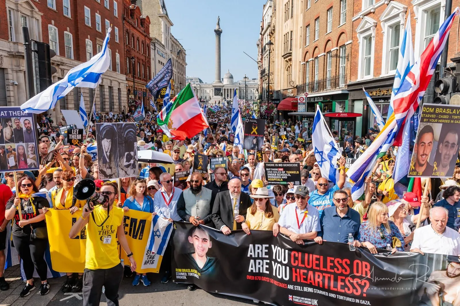 A march fills a sunlit street from side to side and stretches back to Trafalgar Square, Nelson’s Column and the National Gallery behind it, a yellow Let Them Go banner and yellow shirts along the left of the front rank.